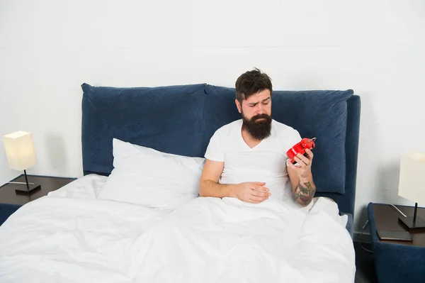 Its hard to get out of bed. Bearded man check time with alarm clock. Sleep time. Sleep and wake routine. Bed time. Bedtime. Morning and night. Regular time to go to bed and wake up