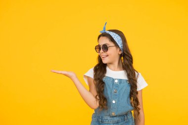 Retro kız ürünü sunuyor. Küçük çocuklar yaz kıyafeti giyer. Neşeli çocuğun klasik bir görünüşü var. Mendil ve güneş gözlüğü - yaz aksesuarı. Güzellik ve moda. Mutlu çocukluk. Boşluğu kopyala