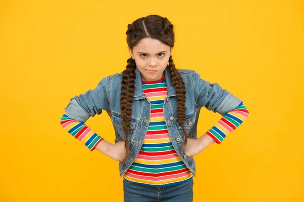 De mau humor. Criança pequena Moody fundo amarelo. O bebé usa penteado trançado. Menina em estilo casual. Um miúdo com as mãos nos quadris. Moda moderna. Tendências elegantes. Cabeleireiro — Fotografia de Stock