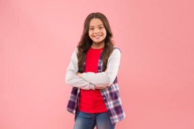 Güzellik neşe veren her şeydir. Küçük güzel gülümseme pembe arka plan. Sevimli bir çocuğun güzel görünüşü. Küçük kız kollarını sıradan bir şekilde kavuşturur. Güzellik ve moda. Çünkü buna değersin.