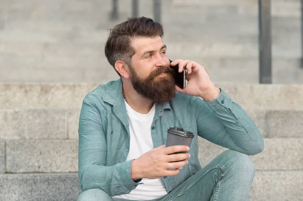 Manteniendo una conversación con una taza de café. El barbudo tiene una conversación telefónica. Respondiendo a la llamada de conversación. Conversación móvil. Descanso. La vida moderna. Nuevas tecnologías — Foto de Stock