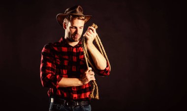 Yakışıklı çiftçi. Batı kovboy portresi. Vahşi batı rodeosu. Siyah şapkalı adam. Kement ipli bir kovboy. Batı. Çiftlikte kareli gömlek. Klasik tarz adam. Vahşi Batı eski kovboy