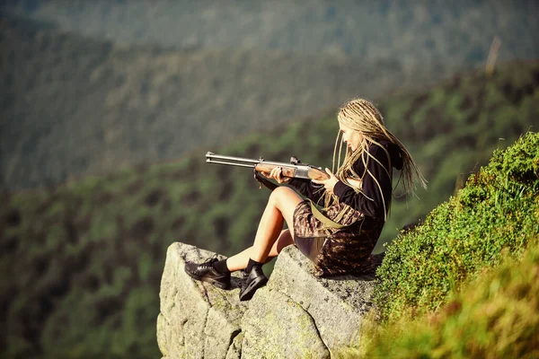 Amazon lány ül a sziklán előkészíti a fegyvert a vadászatra. Célzás koncepció. Vadászidény. Hunter hegyek táj háttér. Szexi harcos. Nő vonzó hosszú haj csinos arc hold puska vadászat — Stock Fotó