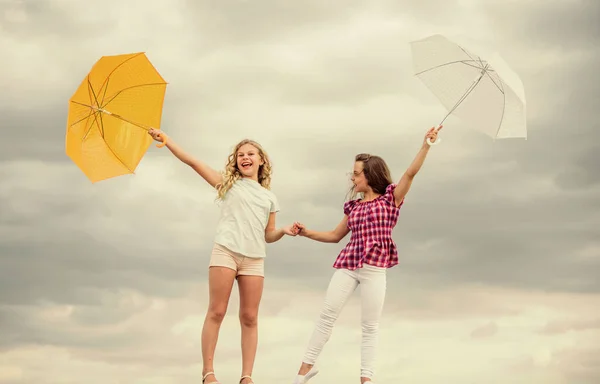 Previsioni meteo. Il tempo cambia. Bambini spensierati all'aperto. Pronti per qualsiasi tempo. Ragazze amiche con ombrelli cielo nuvoloso sfondo. Vento o piovoso siamo preparati. Libertà e freschezza — Foto Stock