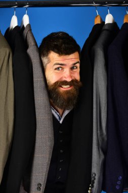 Mavi arka planda özel ceketlerin yanında gülen yüzlü terzi.