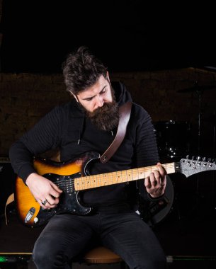 Siyah elbiseli meşgul bir adam gitar tutuyor, çalıyor.