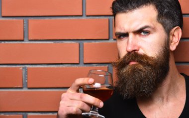 Ciddi yüzlü maço brendi ya da viski içer.