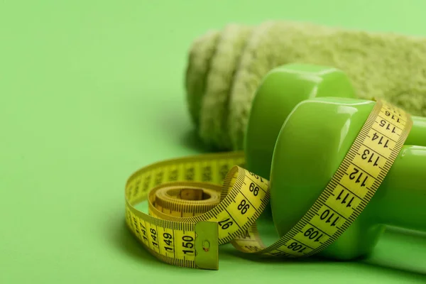 Tape measure in yellow color near barbells, close up