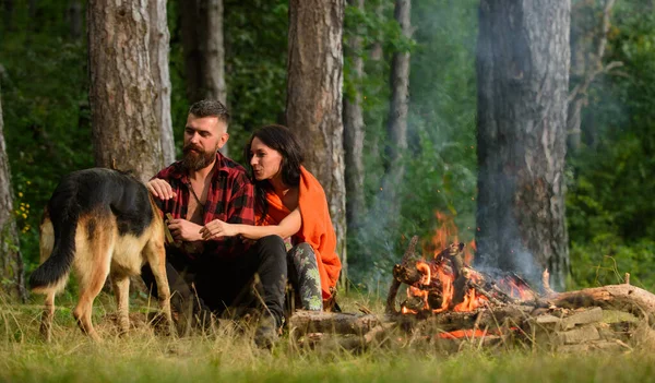 Paar spielt mit Schäferhund am Lagerfeuer, Waldhintergrund. — Stockfoto