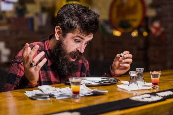 shocked man at table with alcohol drinks, money