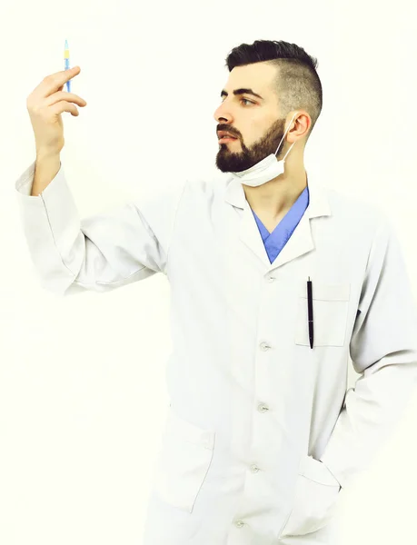 Dentist with beard holds syringe and looks at it attentively — Stock Photo, Image