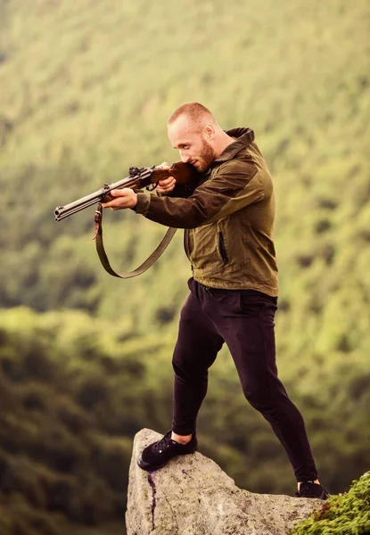 Conceito de caça furtiva. Homem caçador brutal com arma paisagem natural fundo. Caça ilegal. Poacher stand on edge of cliff. Hunter caçador furtivo à procura de vítima. Hunter com rifle ambiente natureza — Fotografia de Stock