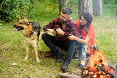 Çiftler şenlik ateşinin yanında Alman çoban köpeğiyle oynuyorlar..