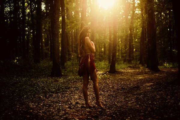 Dangerously sexy. amazon woman. sexy witch. cougar female. sexy girl in leather suede clothes. wild woman in forest. ethnic tribal fashion. deep forest. female silhouette through the sun rays — Stock Photo, Image