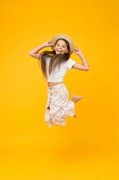 Hasır şapkayla süper aktif çocuk atlayışı. Yalınayak çocuk özgürlüğünü hissediyor. Mutluluk dolu. Yazlık çocuk modası. Küçük kız sarı arka planda yüksekten atlıyor. Enerjik çocuk tatilde. — Stok fotoğraf