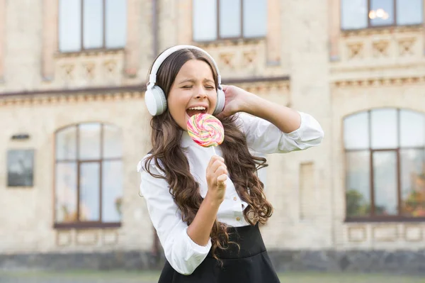 Aku seorang bintang. Gadis dengan headphone. gadis kecil berseragam berkelas makan lolipop. kembali ke sekolah. Pendidikan modern dengan teknologi baru. anak di halaman sekolah. bayangkan dia penyanyi. anak memiliki istirahat musik — Stok Foto