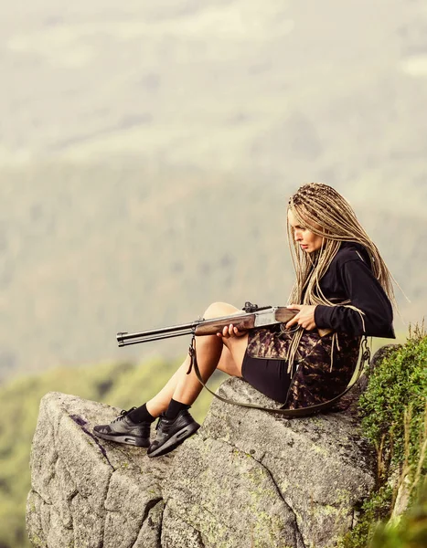 Un guerrero sexy. Mujer atractiva pelo largo cara bonita sostener rifle para la caza. Apuntando al concepto. Chica amazónica sentarse en el acantilado preparar arma para la caza. Temporada de caza. Hunter montañas paisaje fondo —  Fotos de Stock