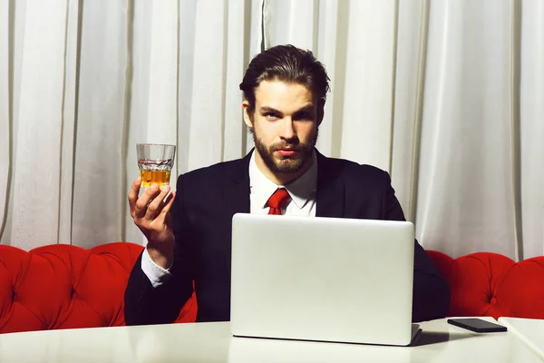 Homem barbudo, homem de negócios segurando vidro de uísque trabalha no laptop — Fotografia de Stock