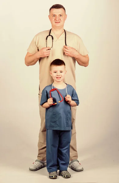 Profesión futura. Quiero ser médico como papá. Lindo niño jugar juego médico. Doctor de familia. Concepto de pediatra. Padre doctor con estetoscopio e hijo pequeño médico uniforme. Medicina y asistencia sanitaria —  Fotos de Stock