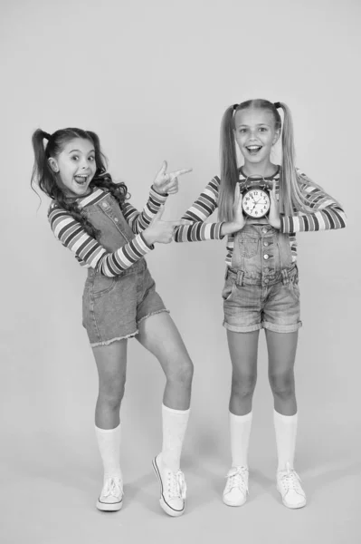 Children break concept. two cheerful girls hold alarm clock. back to school. summertime. discipline and time management. teenage girls yellow wall. children vintage clock. counting for lunch time — Stock Photo, Image