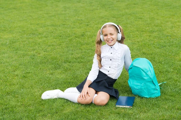 Az oktatás biztonságos. aranyos lány zenét hallgat. Boldog óvodás lány könyvvel az iskola udvarán. Vissza az iskolába. A szorgalmas gyerek fülhallgatót visel. az oktatás fogalma. az online tanulás hétköznapi napja — Stock Fotó