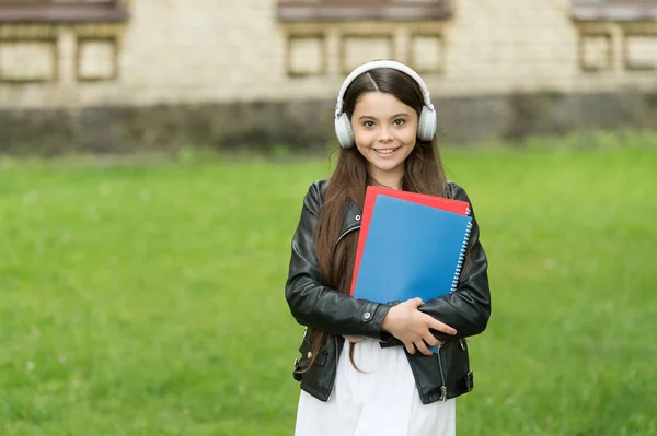 Kde se znalosti setkávají s moderními pomůckami. Šťastné dítě nosí moderní sluchátka venku. Holčičko, poslouchej hudbu. Moderní život. Nová technologie. Moderní učení. Škola a vzdělávání — Stock fotografie