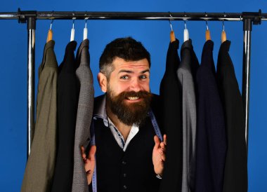 Mavi arka planda özel ceketlerin yanında gülen yüzlü terzi.