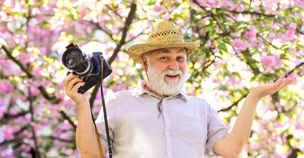Capturing beauty. Photographer in blooming garden. Senior man hold professional camera. Photography courses. Happy grandfather. Travel and tourism. Spring holidays. Travel photo. Retirement travel