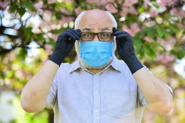 Daha iyi görebilmek için. Parkta sakura çiçeği ağacı. Coronavirus kapanışı sırasında hayat. Hastalık korkusu. Virüsle savaşma stratejisi. Halka açık yerleri ziyaret etmek yasak. Tıbbi maskeli ve eldivenli adam.