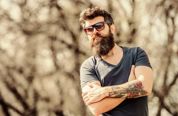 Man bearded with sunglasses nature background. Bearded hipster brutal man wear protective sunglasses. Hipster confident in dark sunglasses. Bearded man wear modern fashionable sunglasses. UV filter