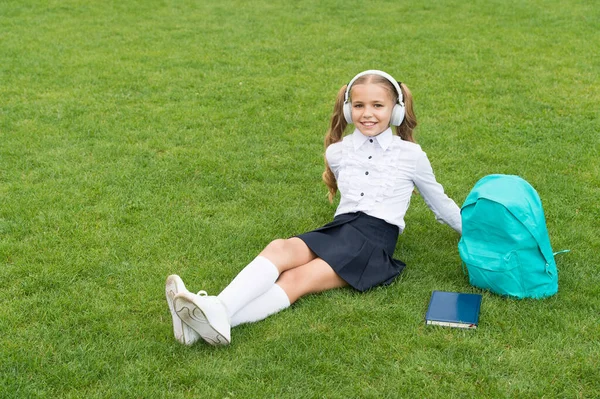 Běžný den online učení. Pěkná holka poslouchá hudbu. šťastná školačka s knihou na školním dvoře. Zpátky do školy. Tvrdě pracující dítě nosí sluchátka. koncepce vzdělávání — Stock fotografie