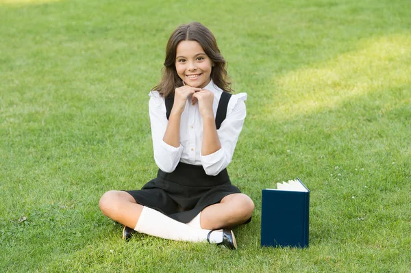 Tradition d'excellence. petit livre de lecture de fille. littérature pour enfants. écrire des souvenirs d'enfance. son journal intime. prendre des notes dans le carnet. retour à l'école. étude d'enfant dans le parc. se détendre sur l'herbe verte avec livre — Photo