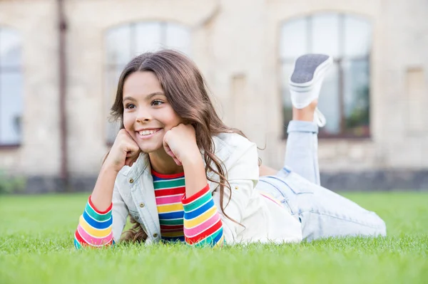 Söka inspiration. liten flicka utomhus. mode för barn. Vår solig dag. Glada skolflicka koppla av på grönt gräs. leende elev barn bära casual stil. Tillbaka till skolan. Glada barnens dag — Stockfoto