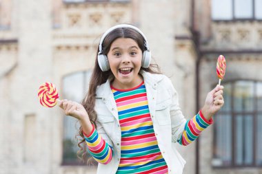 Mutluluk dolu. Havalı hippi kıyafetleri içinde mutlu bir kız öğrenci. çocukluk mutluluğu. Dijital kulaklıklı çocuk. Küçük kız lolipopla müzik dinliyor. Okula dönüyorum. Küçük kız tatlı şeker yiyor