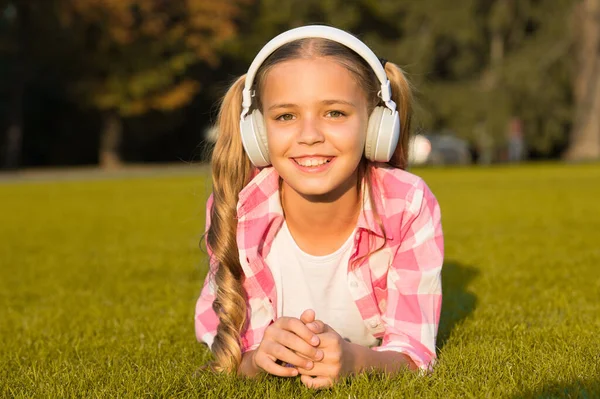 子供のための新技術。幸せな子供の頃の記憶。音楽を聴いてる。学校に戻って。公園で勉強してる。ヘッドフォンで緑の草の上でリラックス。小さな女の子はオーディオブックを聞く — ストック写真