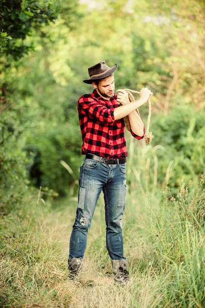 Homem de chapéu segura corda. Ocupações no rancho. Ferramenta de laço. Cowboy americano. Laço amarrado embrulhado. A vida ocidental. Homem cowboy natureza fundo. Dono do rancho. Conceito de criação de Seattle. Cowboy no campo — Fotografia de Stock