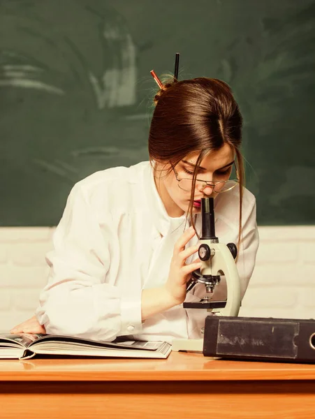 Testy laboratoryjne. Inteligentny student patrzy pod mikroskop w szkolnym laboratorium. Ładna kobieta robi badania laboratoryjne z chemii lub biologii. Dostarczane wraz z nowym, aktualnym sprzętem laboratoryjnym — Zdjęcie stockowe