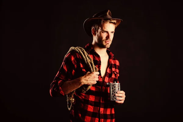 Η ιδέα του Σερίφη. Βίαιος καουμπόι πίνει αλκοόλ. Δυτική κουλτούρα. Αυτός που φοράει καπέλο κρατάει σχοινί και φλασκί. Εργαλείο Λάσο του Αμερικανού καουμπόη. Άνδρας όμορφος αξύριστος καουμπόι μαύρο φόντο. Δυτική ζωή — Φωτογραφία Αρχείου