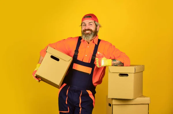 Reparaturen durchführen. Kisten tragen im Gebäude. Umzugskartons auspacken. Neues Haus am Umzugstag. bärtige Bauarbeiter im Anzug halten Kisten in der Hand. Umzug in eine neue Wohnung. Glücklicher Mann Karton — Stockfoto