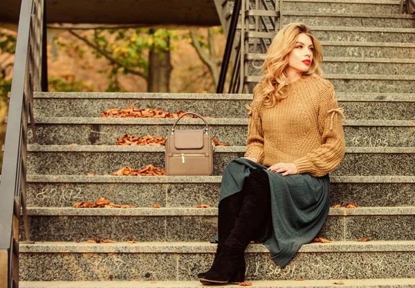 Женщина с роскошной прической сидит на лестнице на открытом воздухе. Осенняя мода. Слой крупногабаритный вязаный поверх девчачьей юбки. Носимые тенденции. Формула осеннего наряда. Как выбрать свитер и юбку на осень — стоковое фото