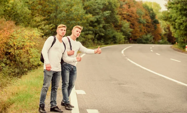 Attraper des promenades. arrêter la voiture avec le pouce levé geste. auto-stop et voiture d'arrêt avec les pouces vers le haut geste à la campagne. Sur la route. Profitant d'une randonnée estivale. Je cherche le transport. jumeaux marchant le long de la route — Photo