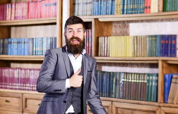 Bearded man in elegant suit smiles and shows thumb up.