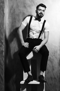 Sakallı adam ciddi yüzüyle sandalyede oturuyor.