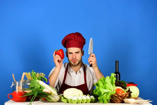 Chef met zelfverzekerde gezicht houdt mes en peper op blauw — Stockfoto