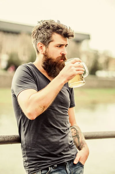 Szakállas és bajuszos férfi sörüveget tart a szabadban. Egy fickó, aki hideg sörrel pihen. Hipster lazán ivott sört a szabadban. Kávézó nyári terasz. Világos vagy sötét sört isznak. — Stock Fotó