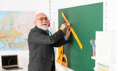 Alıştırma zamanı. Gözlüklü öğretmen, tahtasında cetvelle çizim yapıyor. Okula dönüyorum. Hangi açıdan bakıyorsun? Geometrik şekiller. Lise çağdaş eğitim. Usta öğretmen çizim yaparken cetvel kullanır