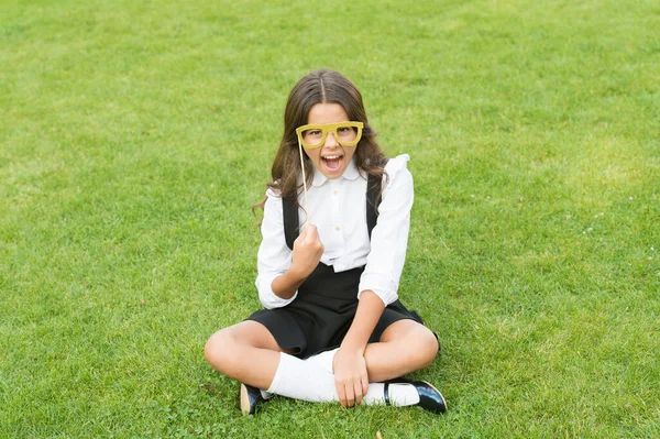 小女孩坐在绿草上.时尚配件。时尚风格。今年摇滚。快乐的女孩拿着护目镜。时装模特的美容美发。小孩校服。回学校去 — 图库照片