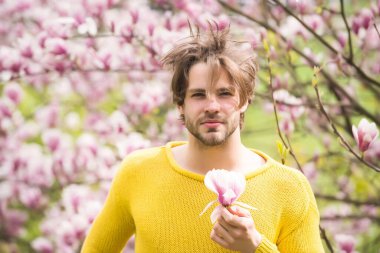 Sakallı, sarı süveterli, çiçekli bir maço.