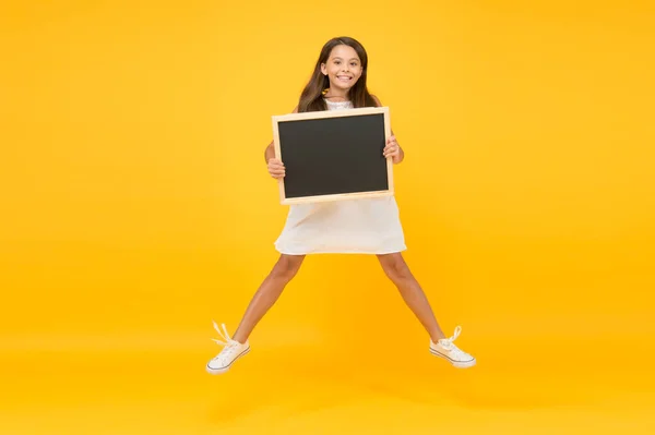 Esta es la vida. vacaciones de verano y vacaciones. Feliz infancia. saltando niña pequeña mantenga pizarra. moda para niños. niño pequeño saltar sobre fondo amarillo. de vuelta a la escuela. espacio de copia. sensación de libertad —  Fotos de Stock