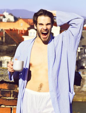 Mavi çizgili pijamalı, elinde fincanla beyaz maço.
